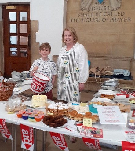 A picture of two volunteers at the cake sale stand with Christian Aid collection buckets